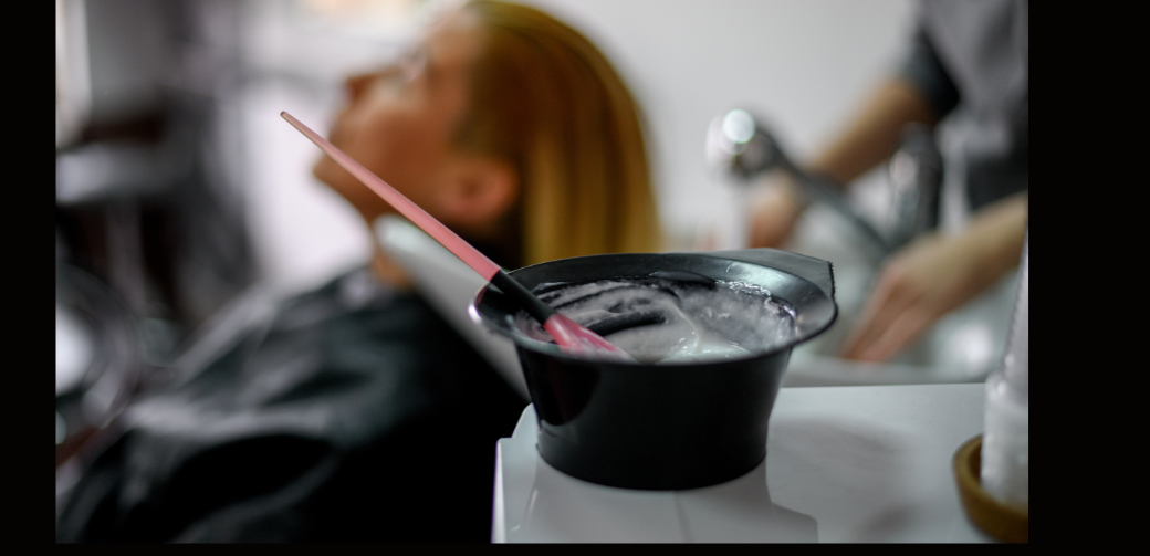 Client with vibrant hair color next to hair coloring product at Othniel Hair Salon, St Pierre, Mauritius.